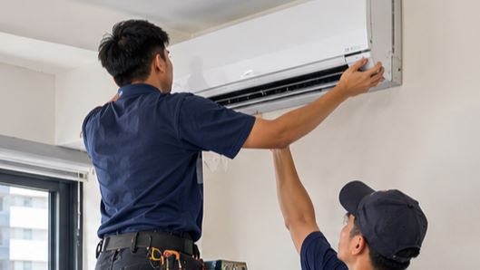 Two technicians mounting a new wall aircon unit in a Penang home
